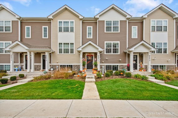 Front view of a row of two-story townhouses with individual entrances and decorative elements on the porches.