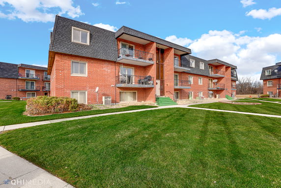 Front view of a multi-story brick apartment building with balconies.
