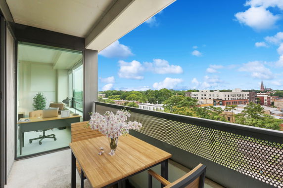 View from a balcony showing a panoramic view of the surrounding buildings and landscape, with a wooden table and vase with flowers in the foreground.
