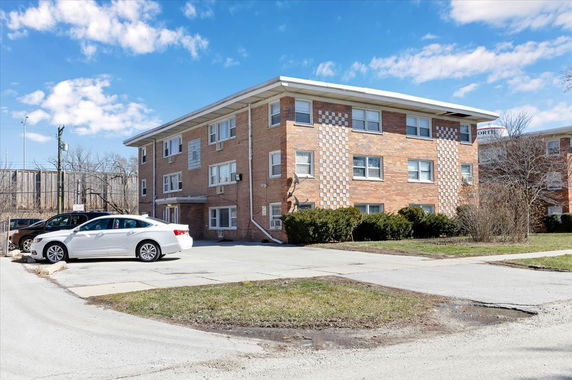 Front view of a three-story brick apartment building with parking area.