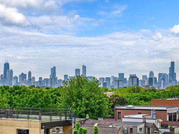 Panoramic view of a city skyline with numerous tall buildings under a partly cloudy sky.
