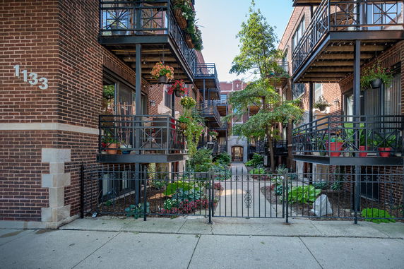 Front view of a multi-story brick apartment building with balconies and a gated entrance.