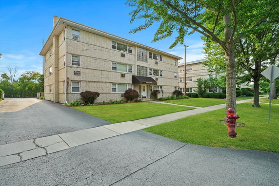 Front view of a multi-story apartment building with a driveway and grassy area.