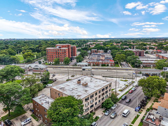 Aerial panoramic view of a neighborhood with various buildings and greenery, including a large red brick building.