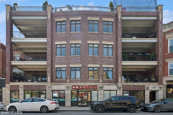 Front view of a multi-story brick building with balconies and commercial space on the ground floor.
