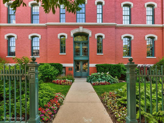 Front view of a red brick building with arched windows and a green entrance gate.