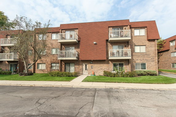 Front view of a three-story brick apartment building with balconies.