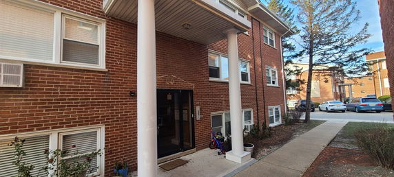 Front view of a brick apartment building with white columns and multiple windows.