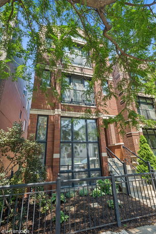 Front view of a multi-story brick building with large windows and a fenced entrance.