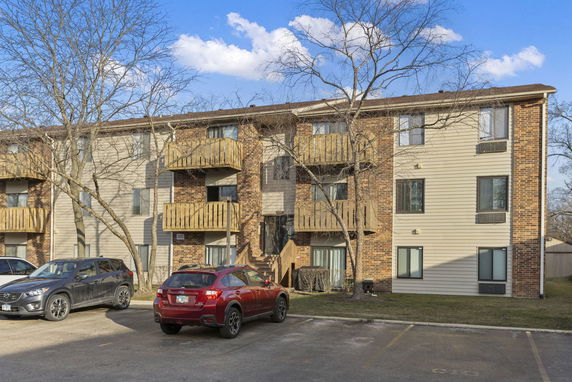 Front view of a three-story apartment building with balconies and a parking area.