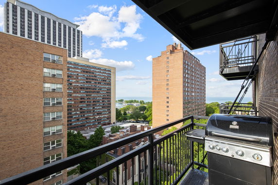 View of surrounding buildings and landscape from a balcony with a barbecue grill.