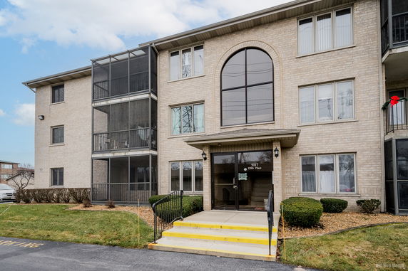 Front view of a multi-story apartment building with a central entrance and screened balconies.