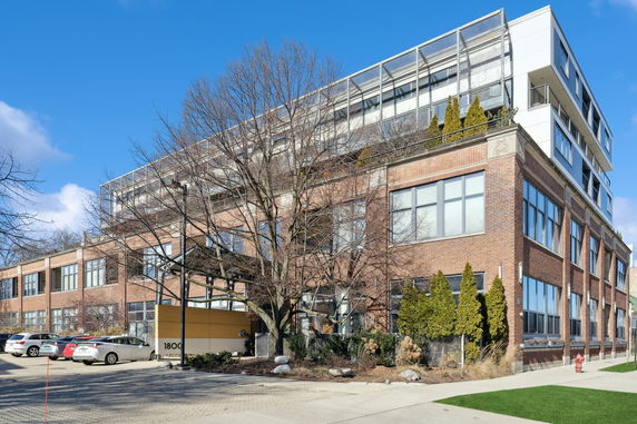 Front view of a multi-story brick building with large windows and a modern upper structure.