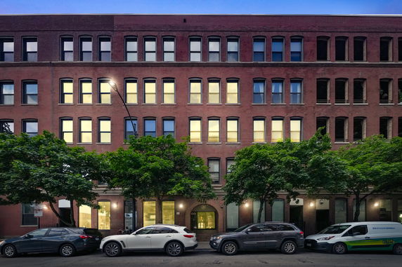 Front view of a multi-story brick building with numerous windows, and cars parked on the street.