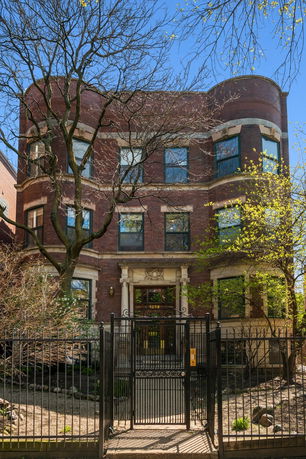 Front view of a three-story brick building with decorative entrance details and a gated front yard.