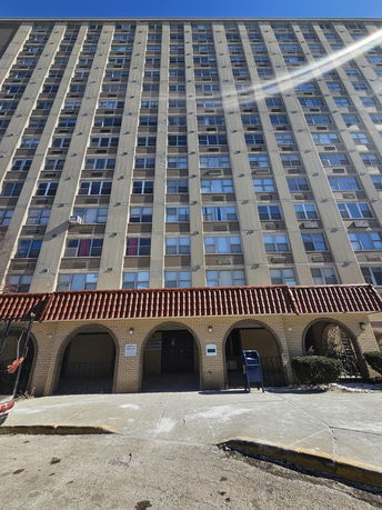 Front view of a tall multi-story apartment building with numerous windows and a tiled entrance area.
