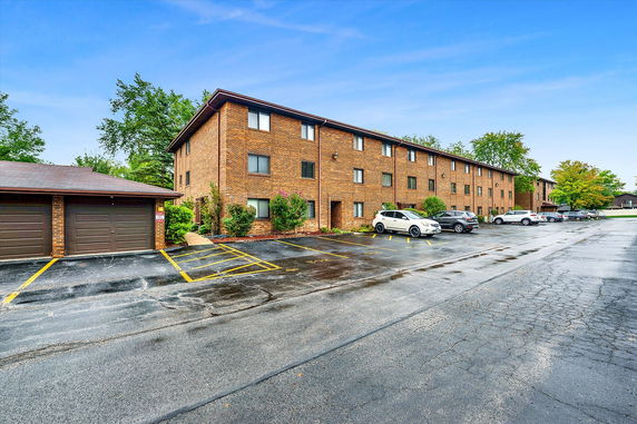 Front view of a multi-story brick apartment building with a parking area.