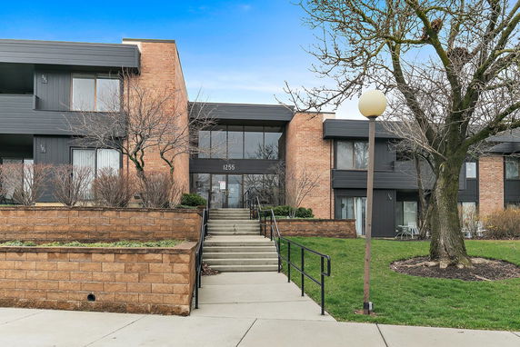 Front view of a building with brick and dark paneling, featuring a stairway entrance.