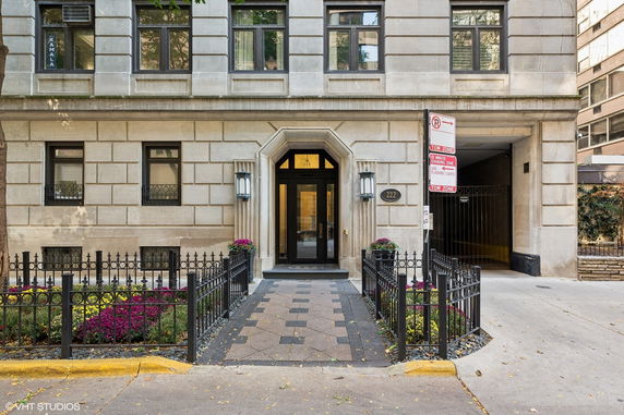 Front view of an apartment building with a gated entrance and stone facade.