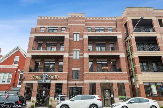 Front view of a multi-story brick building with balconies and ground-level shops.
