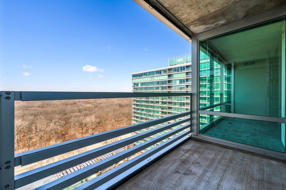 Panoramic view from a balcony overlooking a forest and adjacent modern glass building.