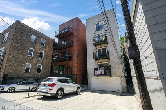 Front view of a brick and concrete multi-story building with balconies and parked cars.