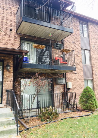 Front view of a multi-story brick apartment building with balconies and outdoor air conditioning units.