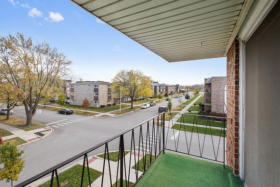 View of residential street from a balcony with multiple apartment buildings and trees.