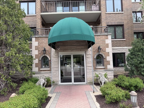 Front view of a multi-story residential building entryway with a green canopy.
