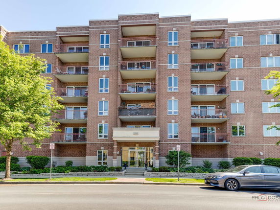 Front view of a multi-story brick apartment building with balconies and large windows.