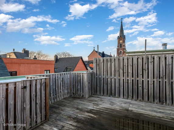 Rooftop with wooden fencing and view of a church spire in the background.