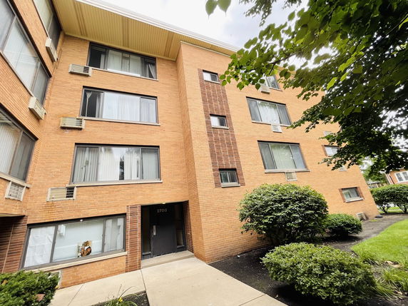 Front view of a multi-story brick building with multiple windows and air conditioning units.
