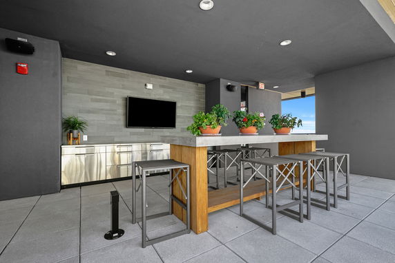 Rooftop area with a bar table, stools, and a TV on the wall.