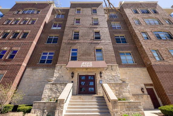 Front view of a multi-story brick building with stone accents and stairs leading to the entrance.