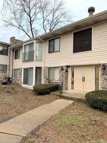 Front view of a two-story residential building with beige siding and a brick facade.