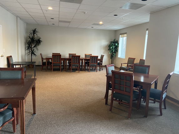 Room with multiple tables and chairs arranged for recreation or meeting activities.