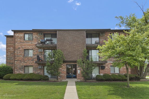 Front view of a three-story brick apartment building with balconies.