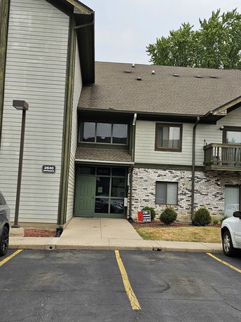 Front view of a multi-story building with a green entrance door and a parking area in front.