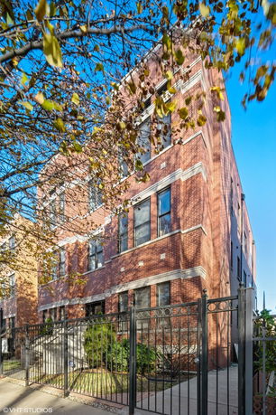 Front view of a multi-story brick building with large windows and an iron fence.