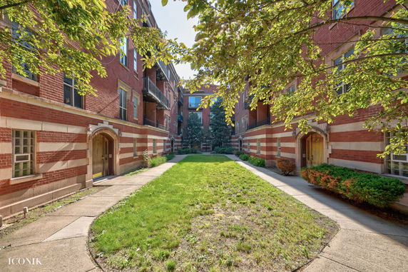 Front view of a red brick apartment building with striped accents and archways.