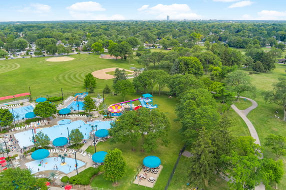 Panoramic view of an outdoor recreational area with swimming pools and slides, surrounded by green fields and trees.