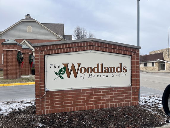 Front view of a building with brick facade and signage for 'The Woodlands of Morton Grove'.