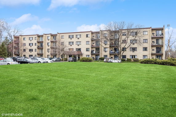 Front view of a multi-story residential building with balconies and a parking area.