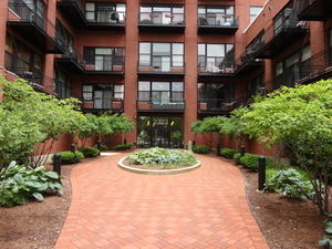 Front view of a multi-story brick residential building with balconies and a garden pathway leading to the entrance.