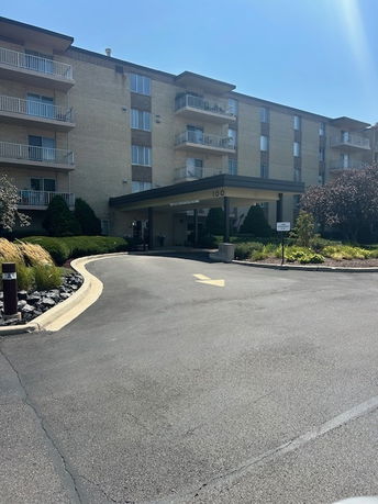 Front view of a multi-story apartment building with balconies and an entrance driveway.