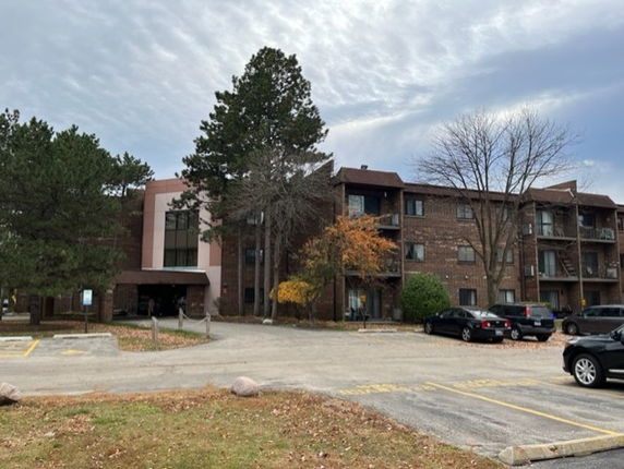 Front view of a multi-story residential building with parking spaces and trees in the foreground.