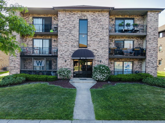 Front view of a multi-story brick apartment building with balconies and an entrance canopy.