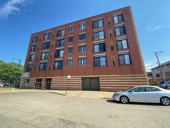 Front view of a multi-story brick building with large windows and an entrance at street level.