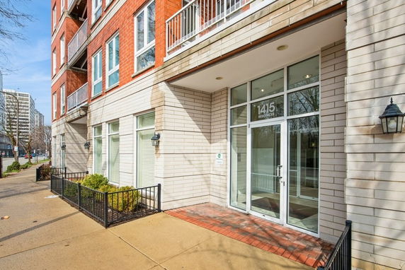 Front view of an apartment building with brick and light stone facade, featuring large windows and a glass entrance.