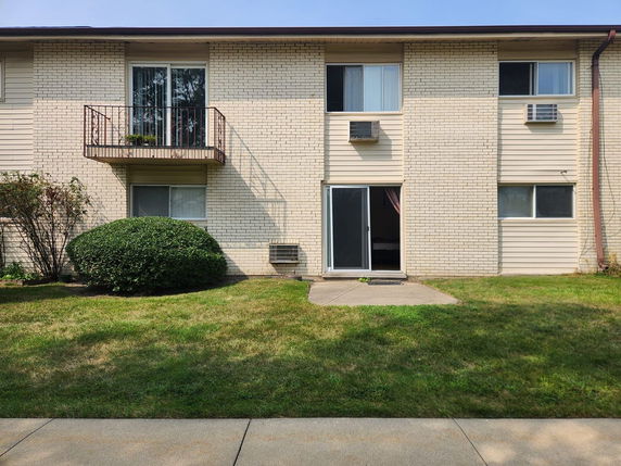 Front view of a two-story building with a small balcony and air conditioning units.